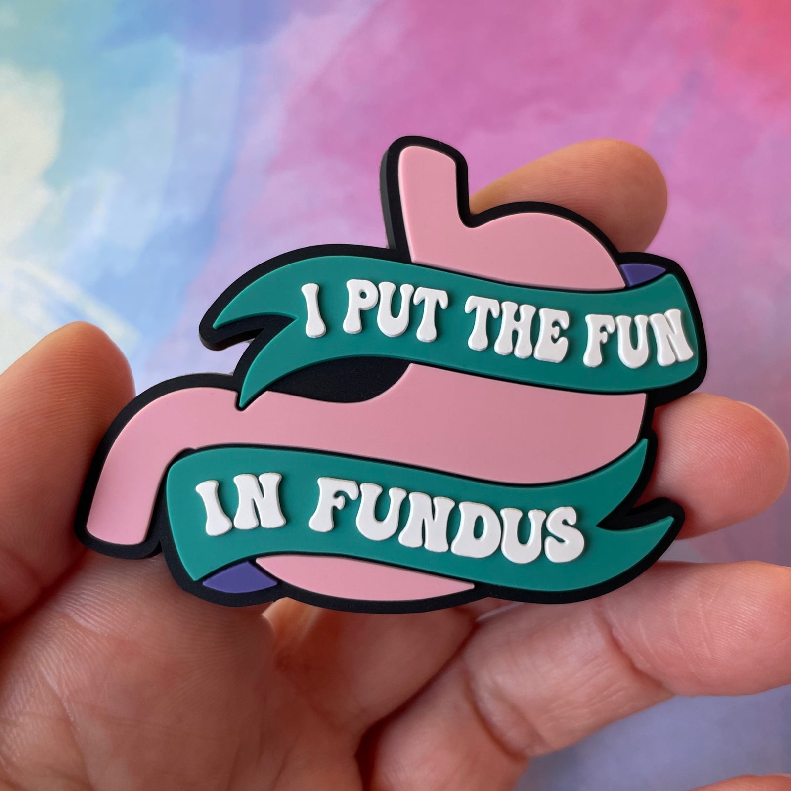 Decorative badge reel with pink stomach graphic and teal banner on a light gray background