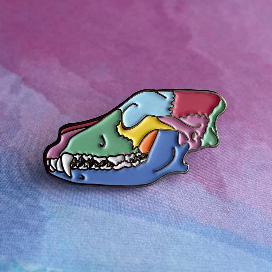 Colorful skull-shaped enamel pin on a light gray background