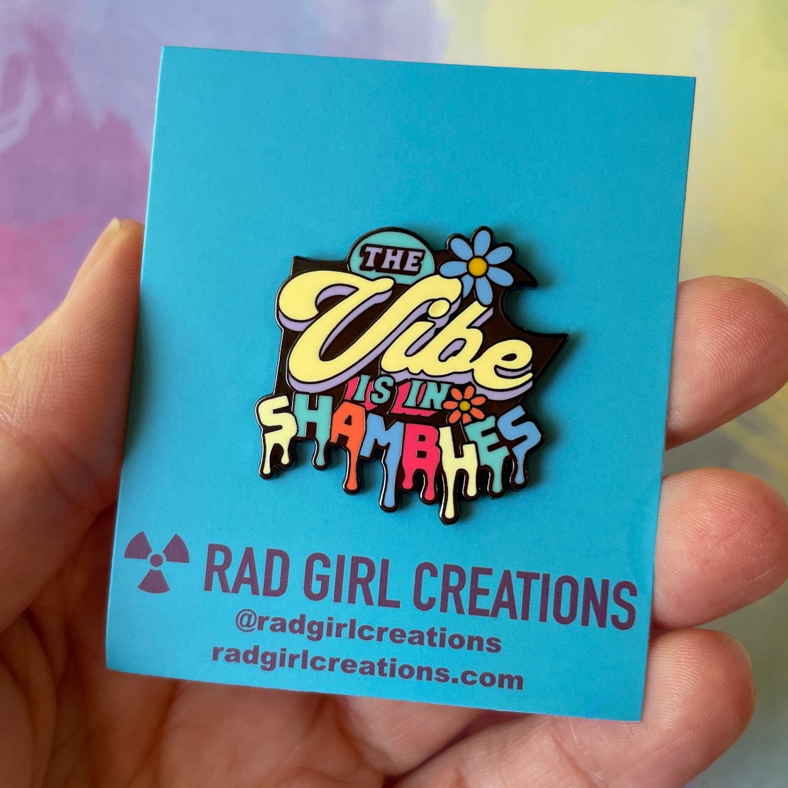 Colorful enamel pin with text and floral designs on a gray background