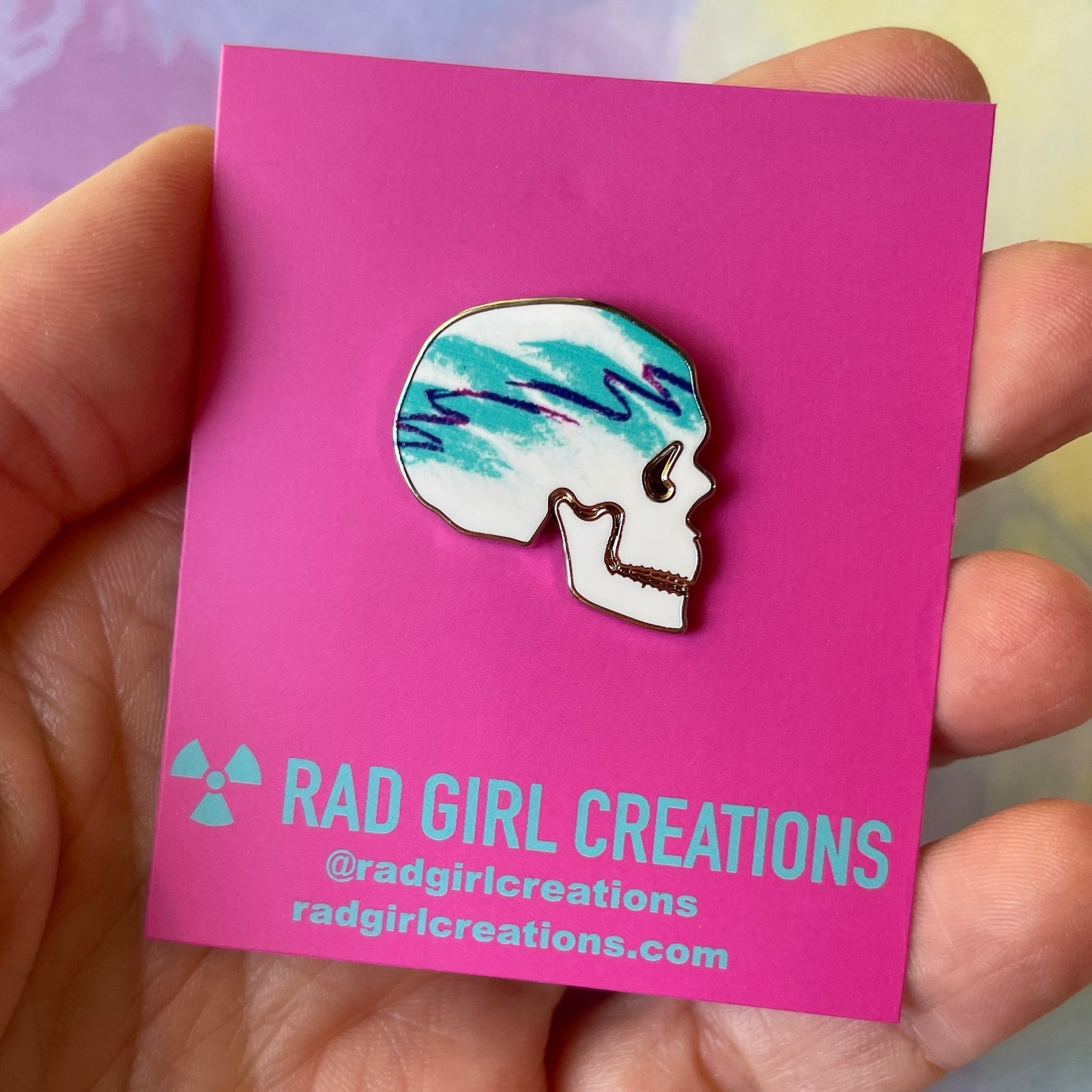 Skull-shaped pin with watercolor design on a gray background