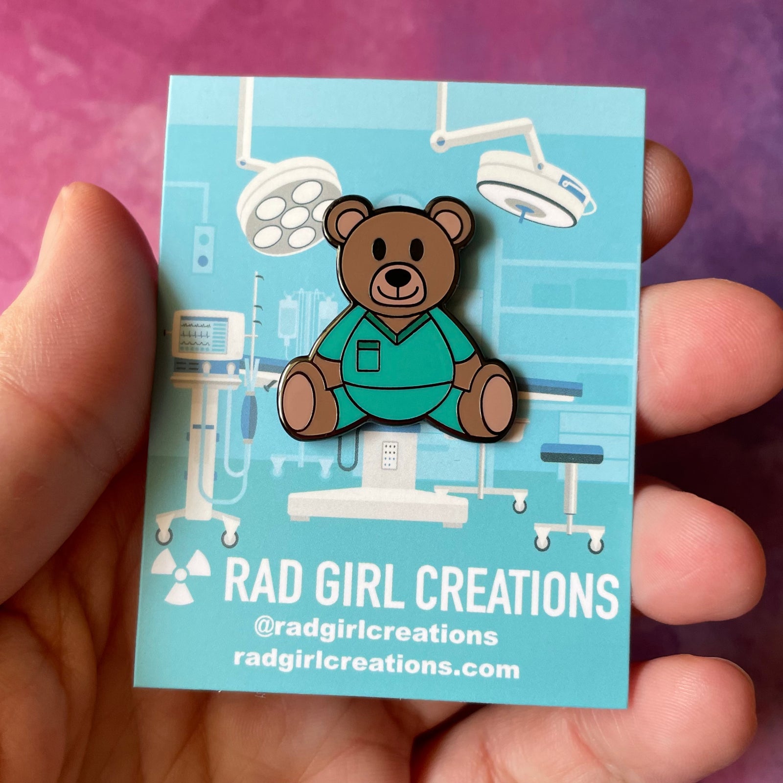 Teddy bear-shaped pin with teal outfit on a light gray background