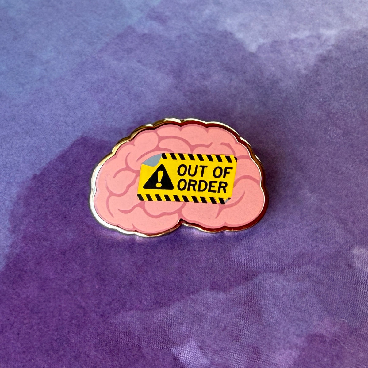 Enamel pin of a pink human brain featuring a yellow 'Out of Order' warning sign with a black exclamation point