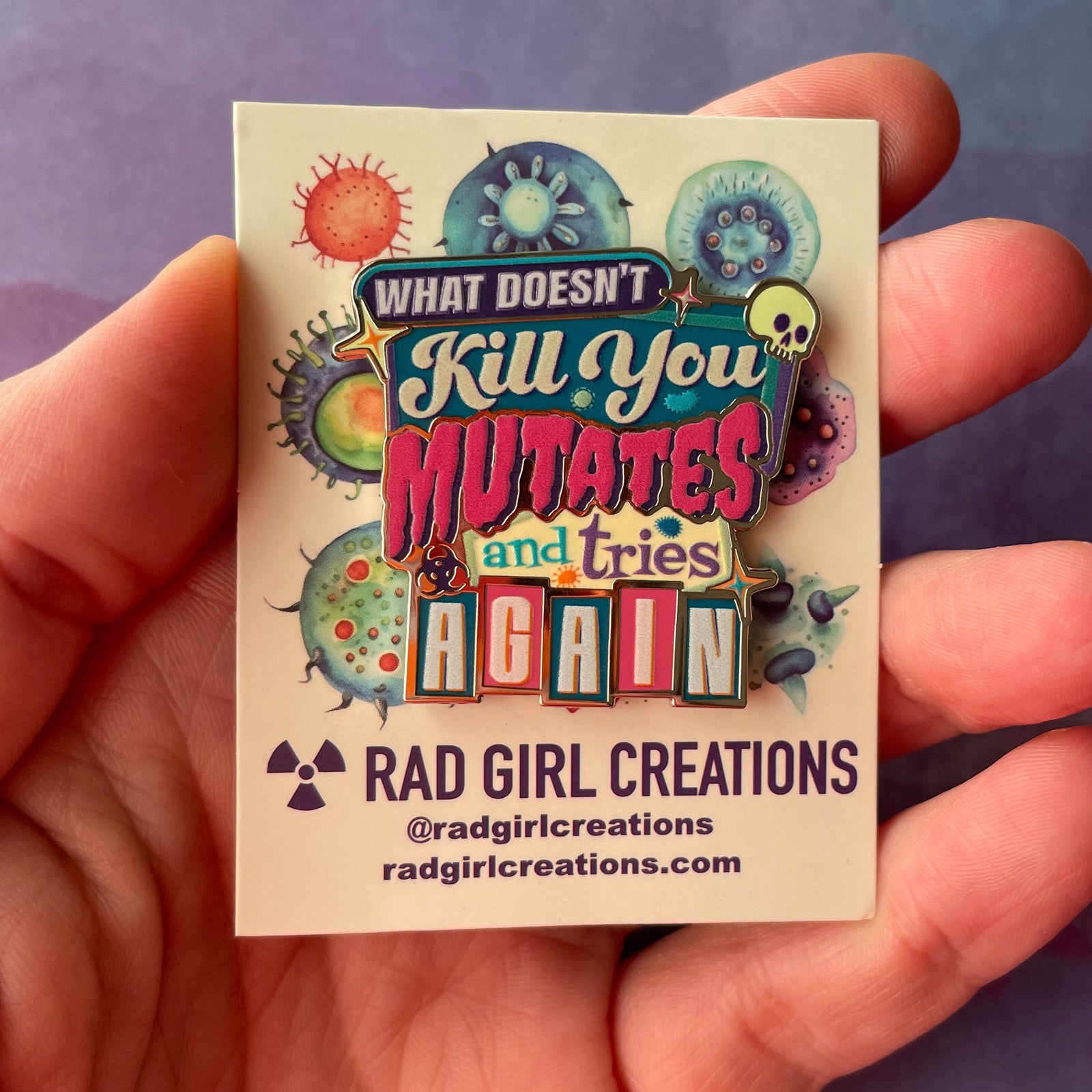 Colorful enamel pin with text 'What Doesn't Kill You Mutates and Tries Again' on a light gray background