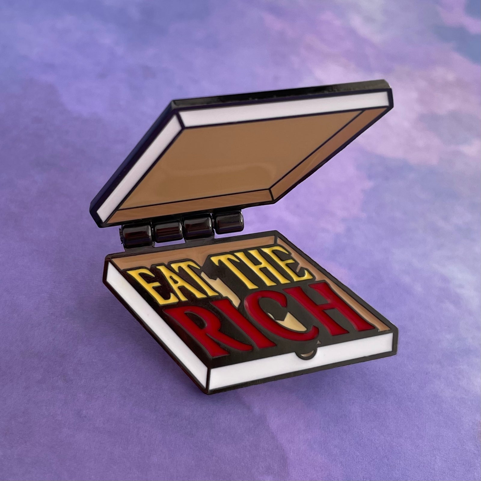 Enamel pin with pizza box design and text on a white background